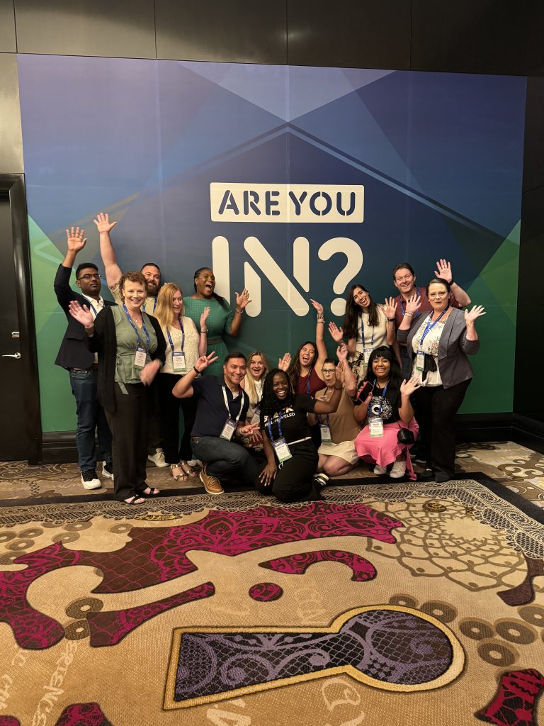 14 expedians with thie hands raised in front of a backdrop that reads "Are you in"